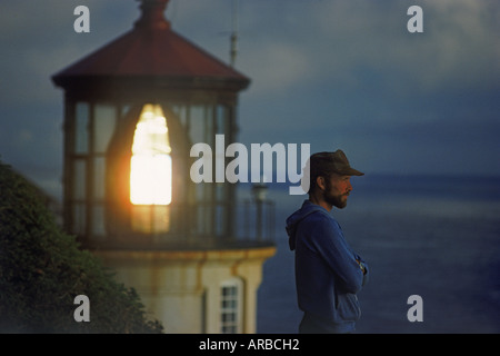 Man standing at dusk on bluff above Pacific Ocean with Heceta Head Lighthouse near Florence, Oregon USA Stock Photo