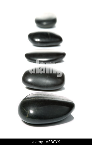 Five black pebbles in a vertical row on a white surface with reflection High key shot Stock Photo