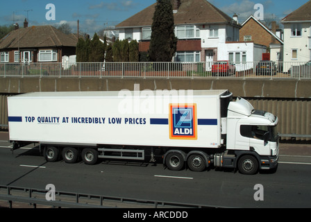 Aldi supermarket lorry on trunk road in cutting below residential dwellings with separate service road shows retaining wall Stock Photo