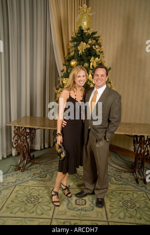 An attractive young couple pose for a formal picture in front of a Christmas tree Stock Photo