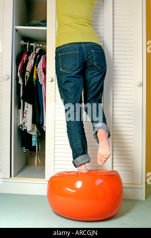 Young woman on a stool looking for clothes in her wardrobe. Stock Photo