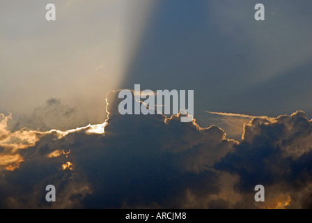 Evening sun shining from behind bank of clouds and projecting rays over the sky Stock Photo