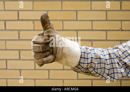 Thumbs up - a hand in a worn and dirty work glove gives the thumbs up sign against a brick wall background Stock Photo