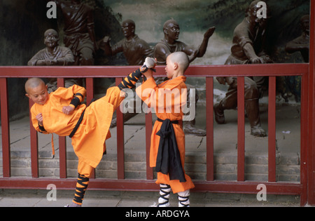 Two young kung fu students in bright orange robes practice their kicks inside the Shaolin Temple Stock Photo