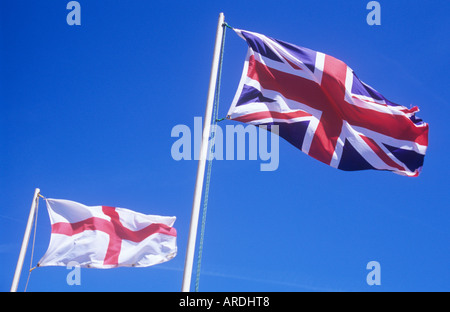 St George flag or English Ensign fluttering from flagpole against clear blue sky with Union Jack on separate pole Stock Photo