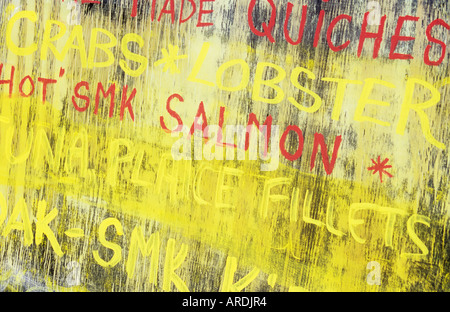 Blackboard outside fish shop which has lost most of its black and is stained yellow with chalk advertising fish varieties Stock Photo