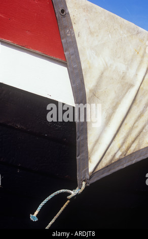 Detail of white tarpaulin stretched over the hull of a large red white and black painted boat under a blue sky Stock Photo