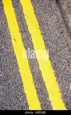 Diagonal detail from above of freshly painted double yellow lines on tarmac road with kerb Stock Photo
