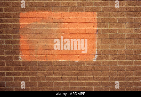 Part of a featureless ugly brick wall with a patch of non-matching red paint attempting to obscure graffiti Stock Photo