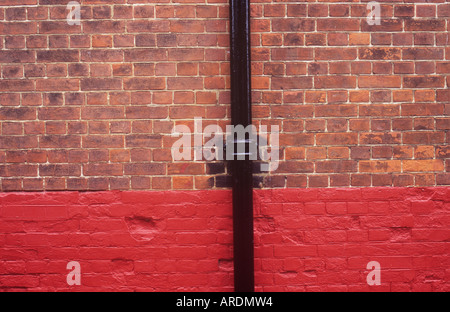 Detail of dark red brickwall the lower third of which has been painted a fresh red and with a newly painted black drainpipe Stock Photo