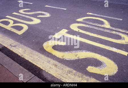 Angled view from pavement and kerb of well worn letters and lines painted in yellow on road surface stating Bus Stop Stock Photo