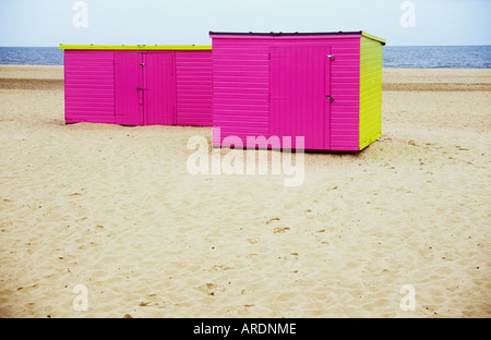 View of deserted dry white sandy beach with footprints and two pink and lime green sheds perched on it Stock Photo