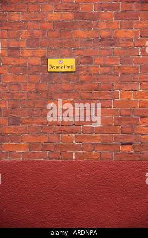 Weathered dark red brickwall the lower part of which has been stuccoed and painted red with no parking At any time sign Stock Photo