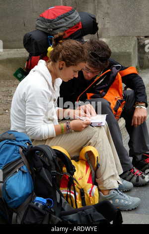Young backpackers sitting on the roadside reading a tourist guide book. Stock Photo