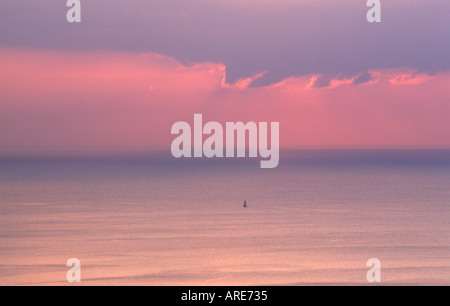 Lone yacht sailing across calm open sea ocean in evening morning light Stock Photo