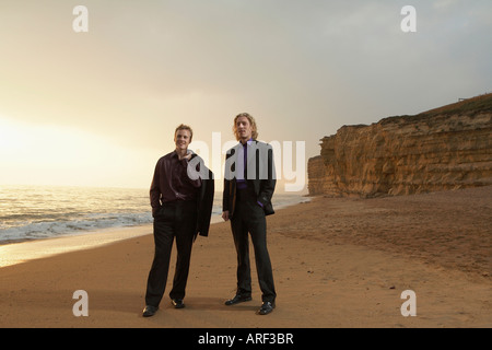 Two men standing on beach at sunset Stock Photo