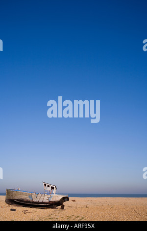 Old weathered fishing boat on a pebble beach in Dungeness, Kent on a summers blue sky day Stock Photo