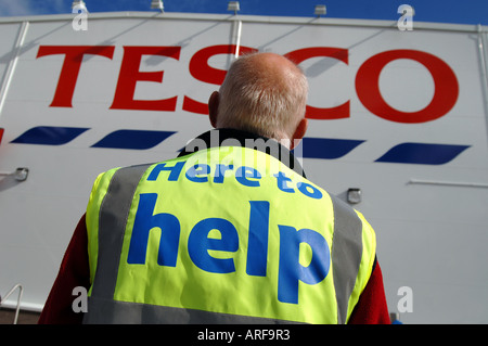 An elderly man working for tesco supermarket in Ilfracombe, Devon, standing outside the sign of the store. Stock Photo
