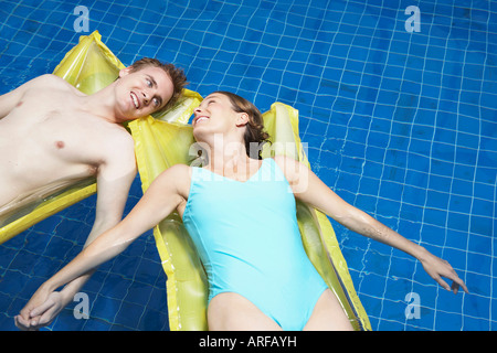 Couple lying on lylos holding hands Stock Photo