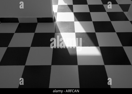 A black and white tiled floor, with a shaft of sunlight shining diagonally across it. Stock Photo