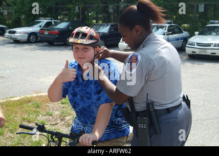 Prince George's County policewoman  fixes a helmet on bicyclist while he gives the thumbs up approval  sign Bowie, Maryland Stock Photo