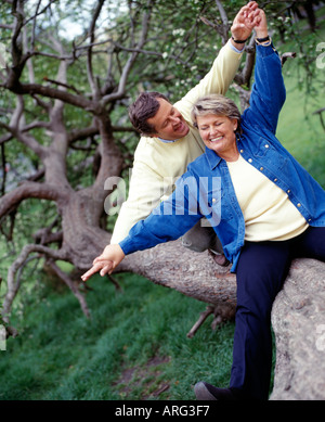 middle aged couple sitting together having fun on tree trunk Stock Photo