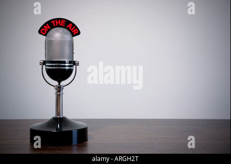 Retro microphone with an On the Air illuminated sign on a desk vignetted background Stock Photo