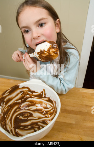 Little girl licking chocolate from bowl off spoon after baking Stock Photo