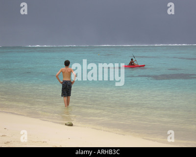 Rear of a young man standing on a beach watching a boat on the sea Moorea Tahiti French Polynesia South Pacific Stock Photo