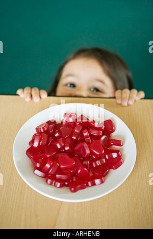 Girl looks up at plate of heart shaped sweets on a table Stock Photo