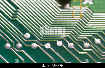 Macro view of a green printed circuit board (PCB) showing gold conductive traces and silver solder pads. Detailed electronic engineering background. Stock Photo