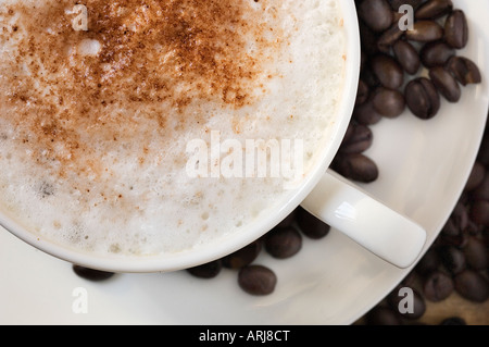 A close up of freshly made cup of Cappuccino coffee on a saucer, surrounded by roasted coffee beans Stock Photo