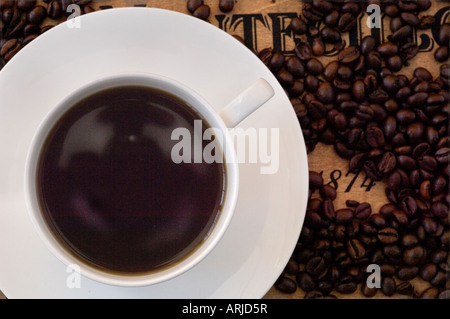 A close up of freshly made cup of coffee on a saucer, surrounded by roasted coffee beans on a antique wooden surface Stock Photo