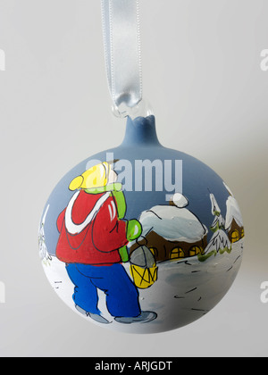 Traditional festive Christmas  bauble glass ball decoration  with a child in the snow and  snow covered houses in blue and Stock Photo