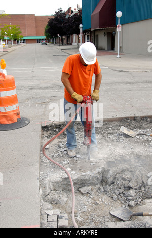 Road repair construction site with heavy equipment and man wearing a hard hat for protection using a jackhammer Stock Photo