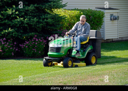 Senior man mows lawn on a riding grass cutting mower Stock Photo