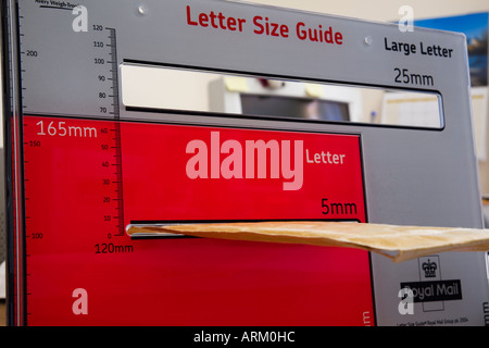 USING ROYAL MAIL LETTER SIZE GUIDE with brown envelope being measured in small 5mm thickness on red section for standard Stock Photo