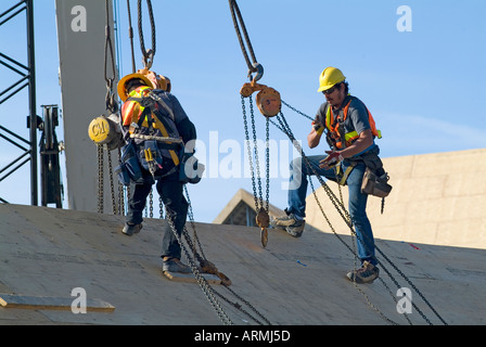 Workers on a roof of a housing development wear special protective clothing and helmets Stock Photo
