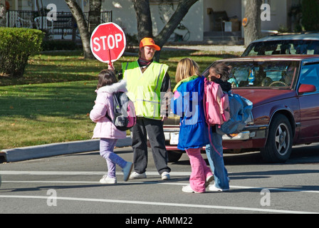 Elementary school crossing guard provides safety to children crossing busy streets roads highways while walking home from school Stock Photo