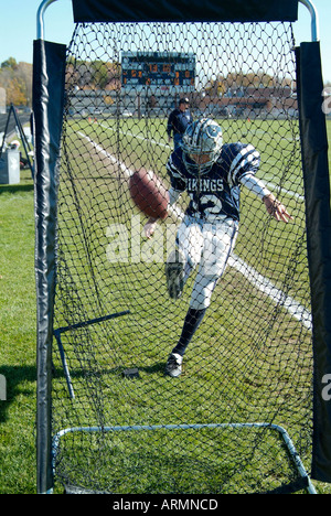 Football player practices kicking football into a net prior to ...