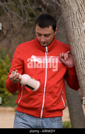 drunken young European man in park holding bottle of alcohol Stock Photo