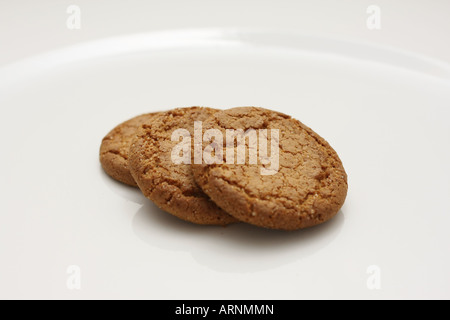 Three gingernut biscuits on arranged on a white plate Stock Photo