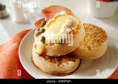 Hot uttered Crumpets with melted grilled brie or camembert or goats cheese and capers, served on a white plate in a table setting Stock Photo