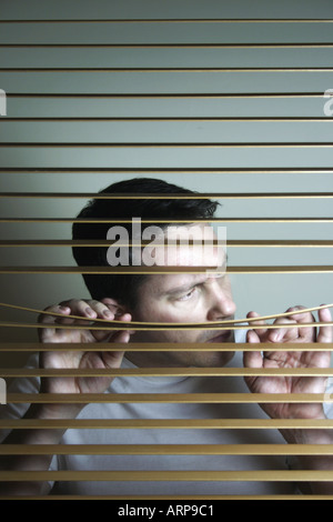 Man looking out from behind window blinds Stock Photo