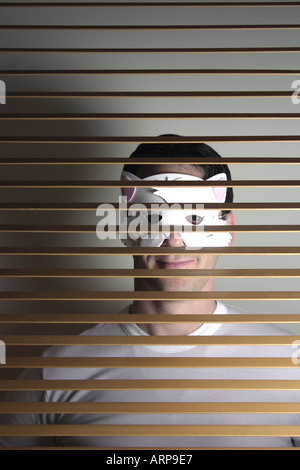 Man with cat mask behind window blinds Stock Photo