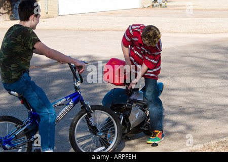 A teenage boy sits on his bicycle and looks on as his friend refruels his motorized pocket bike. Stock Photo