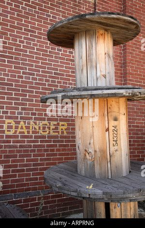 Large empty wooden reels used to hole cable next to brick wall with the word DANGER printed on it. Stock Photo