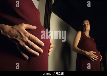 Pregnant woman looking at herself in a mirror and contemplating her future child. Stock Photo
