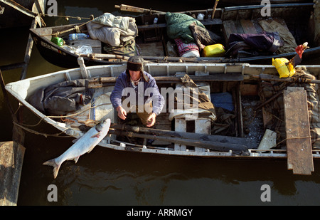 A fishermen is throwing a fish to a customer waiting on the shore Stock Photo