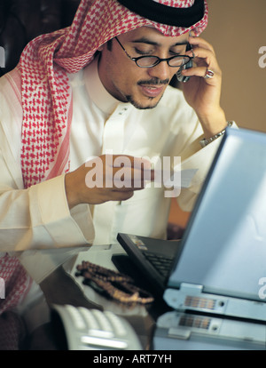 Saudi businessman using mobile phone and laptop in his office Stock Photo